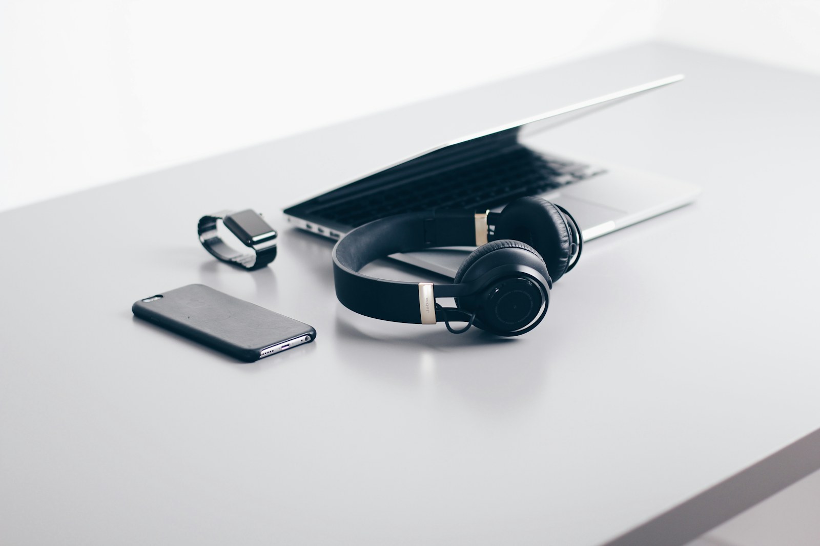 Over-ear headphones, smartphone, smartwatch, and laptop on a clean white desk