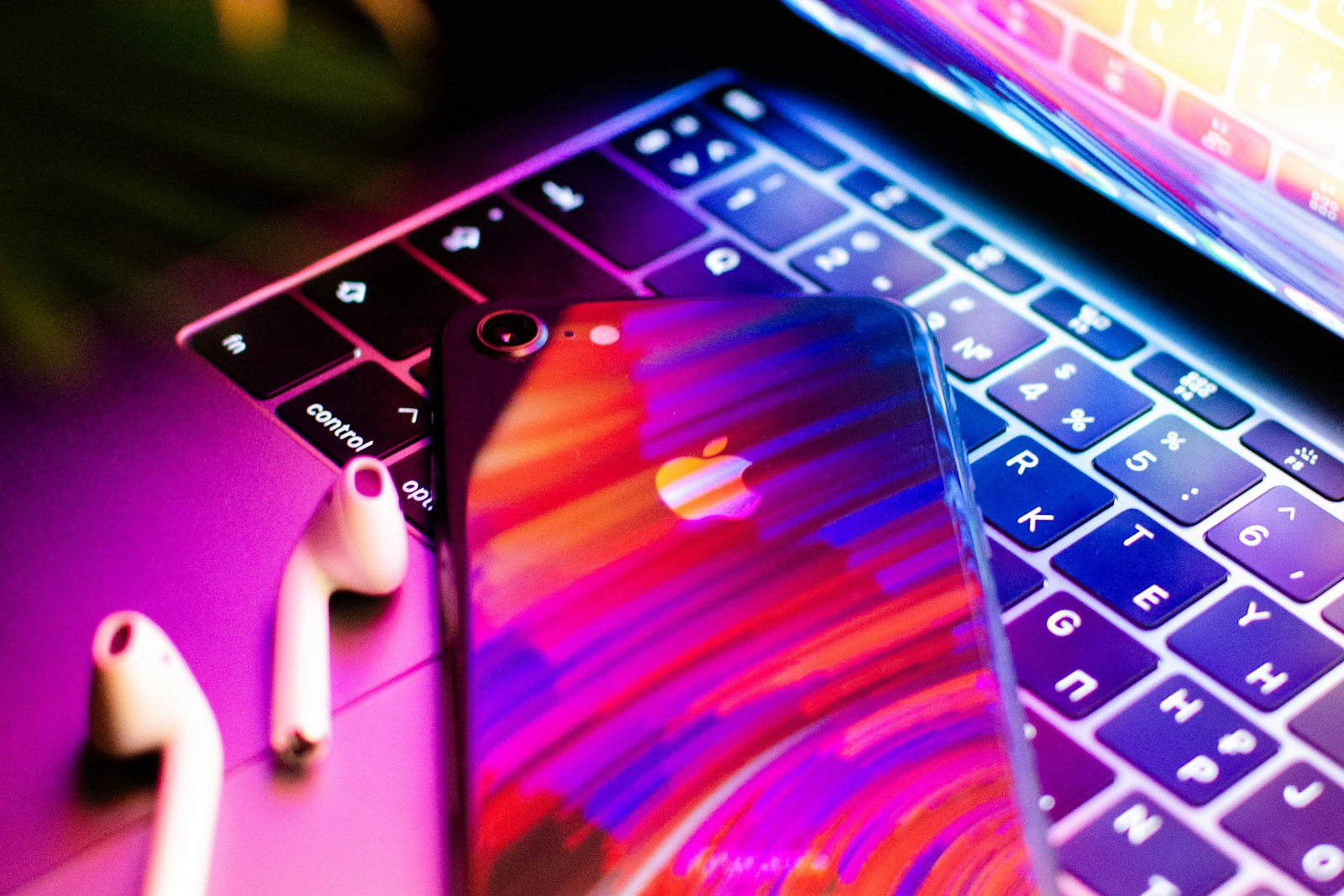 Smartphone and wireless earbuds resting on a colorful illuminated laptop keyboard