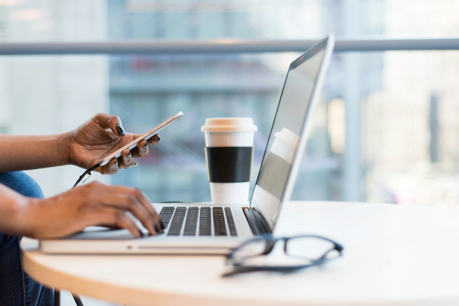 Person using a smartphone while working on a laptop at a café table
