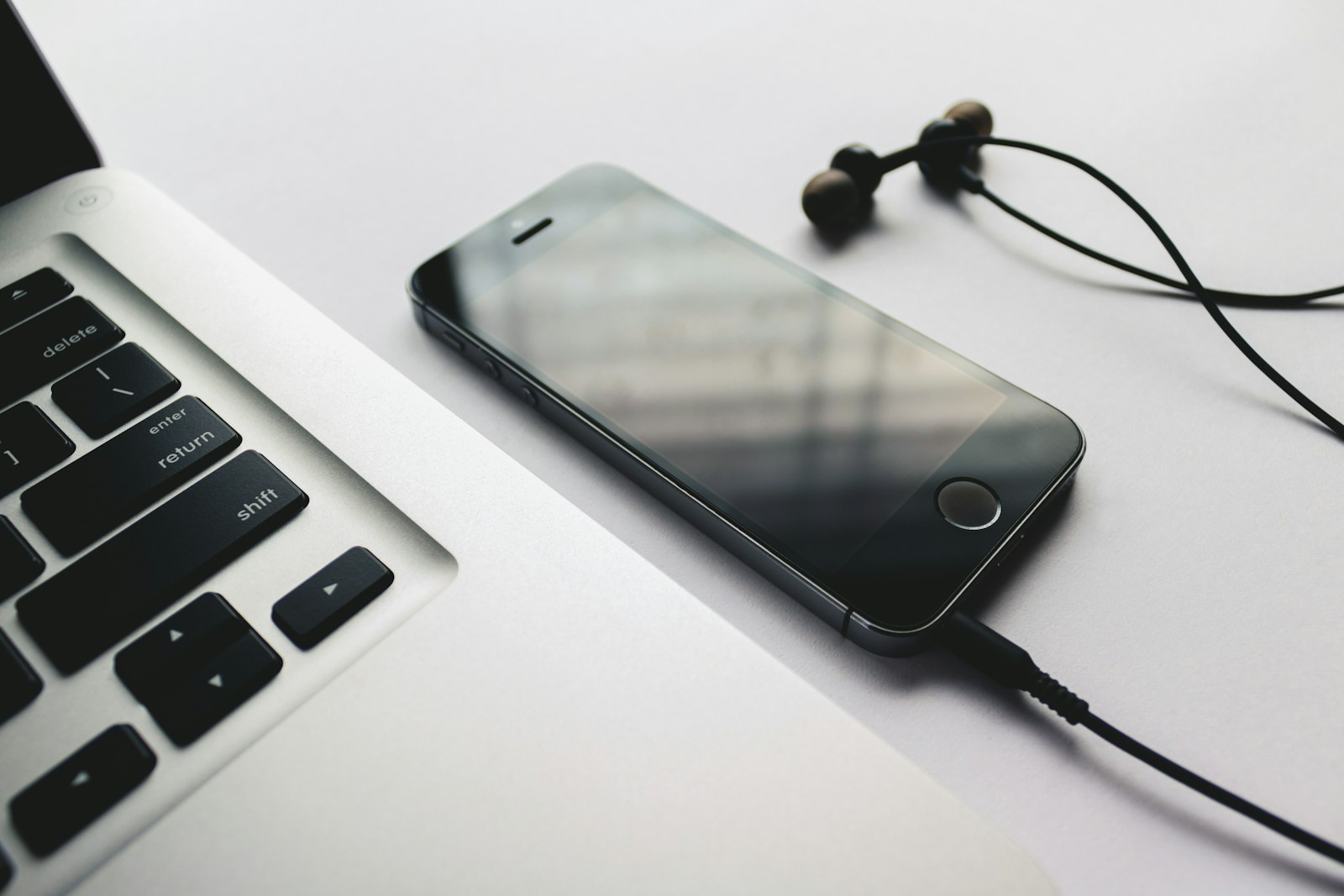 Wired earphones and smartphone beside a laptop on a desk