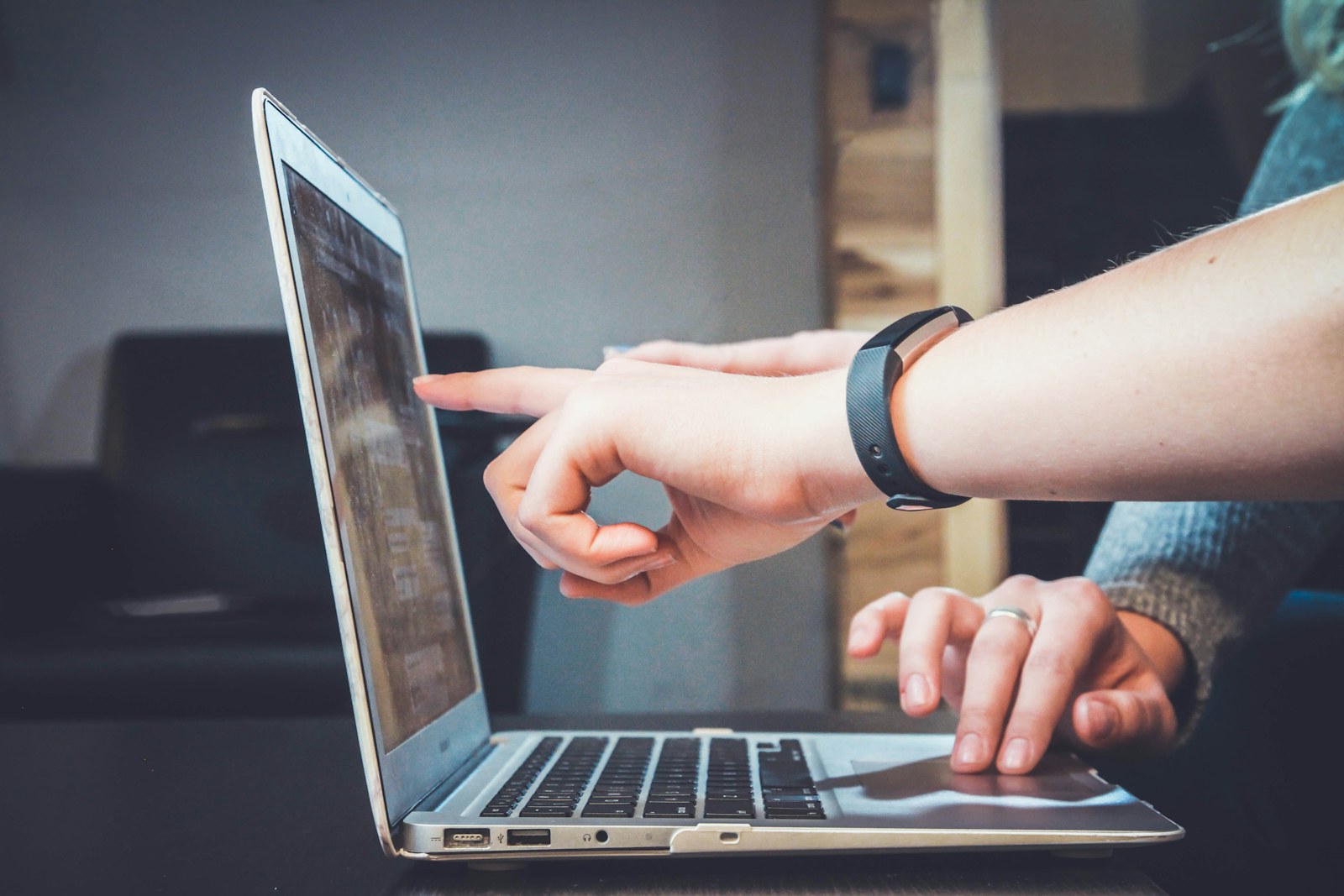Two people collaborating around a laptop while one wears a fitness tracker